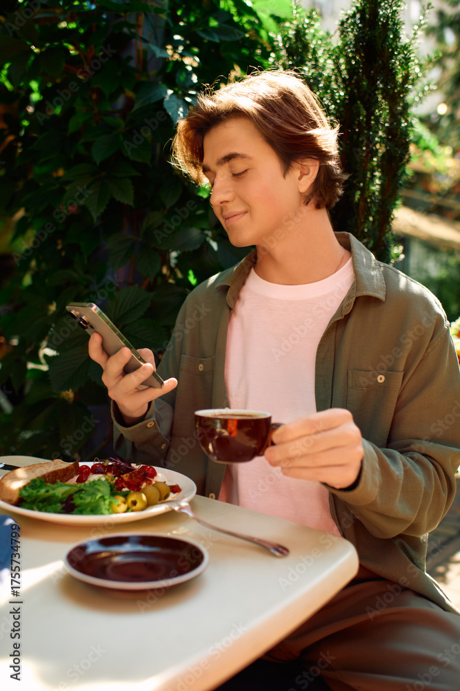 Fototapeta premium Young man enjoys a meal while checking his phone at a cozy modern cafe