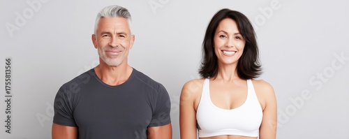 Athletic couple, a middle-aged man and woman, smiling confidently in fitness attire, showcasing healthy lifestyle choices and positive energy in a bright, minimalistic studio environment