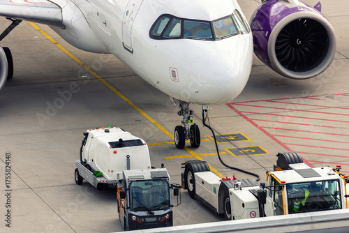 Modern regional  jet aircraft airport tarmac connected to ground vehicles for refueling maintenance. Engine cockpit clearly visible crew performs technical operations before next scheduled flight