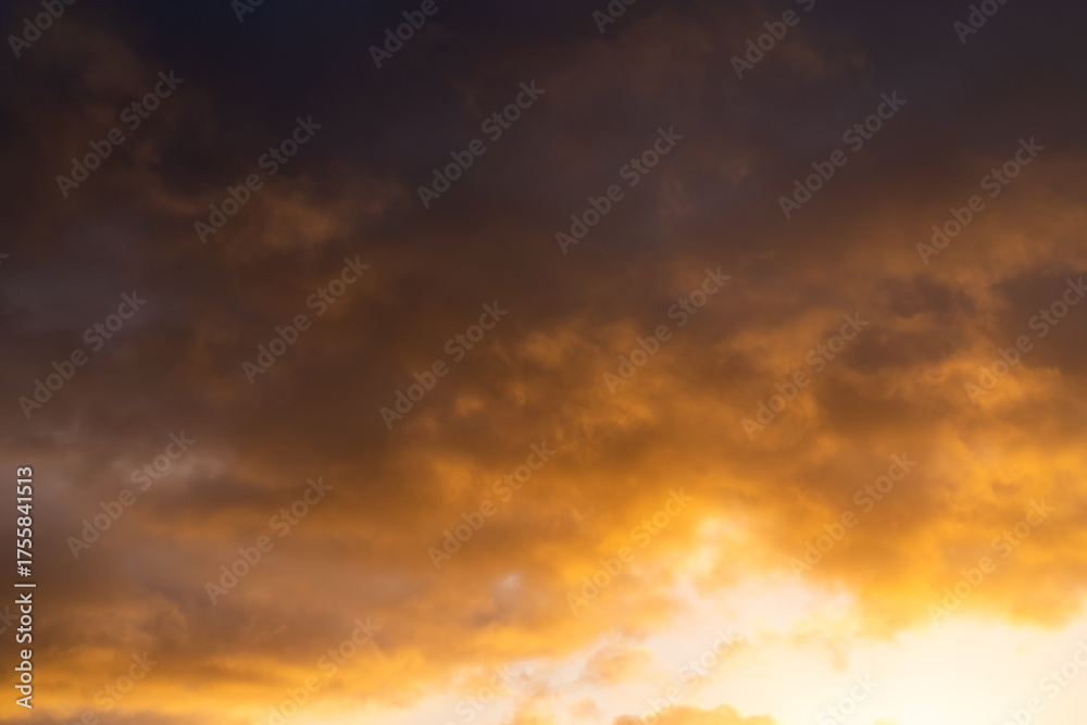 Obraz premium Warm golden light illuminating dramatic clouds at sunrise creating a moody and atmospheric sky