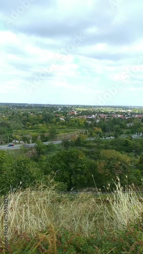 Petrovaradin from fortress wall: greenery, low houses with red tile roofs, cloudy sky atmosphere. Concepts of cozy European townscape, Serbia heritage exploration, and historic district architecture.