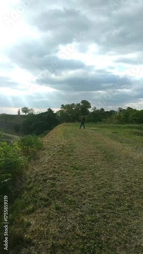 Traveler walking across Hornwerk grassy area and ramparts of Petrovaradin Fortress, video from a distance. Concepts of old military site discovery, solo travel adventure, sustainable heritage tourism.