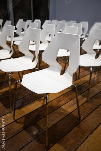 Modern white chairs arranged neatly on a polished wooden floor, ready for a conference or event, creating a clean and professional aesthetic.