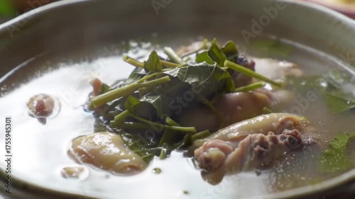 Steaming clear broth with chicken pieces and green herbs in a rustic ceramic bowl, close-up shot