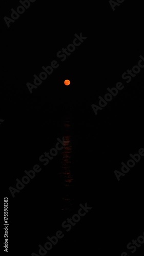 Strawberry full moon vertical video. Atmospheric nighttime video of moon reflection in water. Conceptual mystical time. A bright orange moon path in a dark sea. Moonrise over the horizon. Astrology
