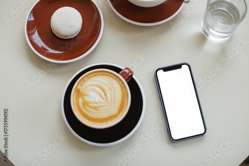 Papier peint Overhead view of a mobile phone with a blank screen, a cappuccino and french macaroon on a table