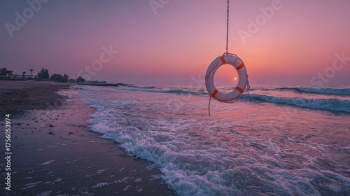 A life preserver hangs on a chain at a pink sunrise seaside view. This beautiful beach scene shows safety, hope, and peaceful tranquility.