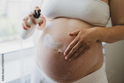 A pregnant woman applies skincare cream to her skin. This moment emphasizes self-care during pregnancy.