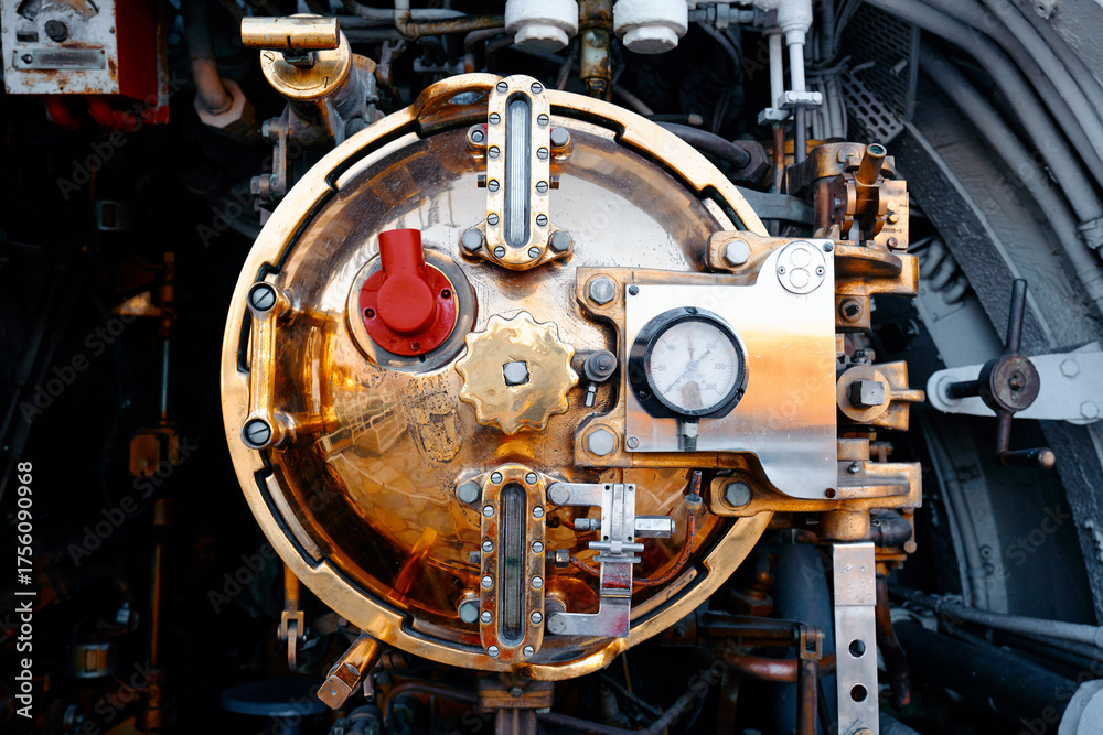 Fototapeta premium Close-up of brass-coated steam engine door with dials, gauges, and levers on an old locomotive. Rich metallic tones convey industrial craftsmanship, precision, and vintage railway technology.