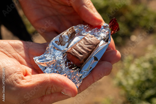 Εκτύπωση καμβά Chocolate bar or chocolate candy is held in hands with shiny wrapper in outdoor