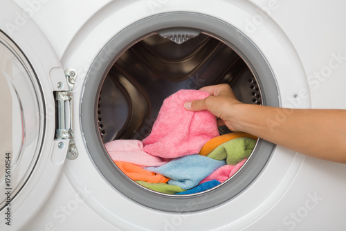 Young adult woman hand holding and unloading colorful soft microfiber cleaning rags from opened white washing machine. Closeup. Front view.