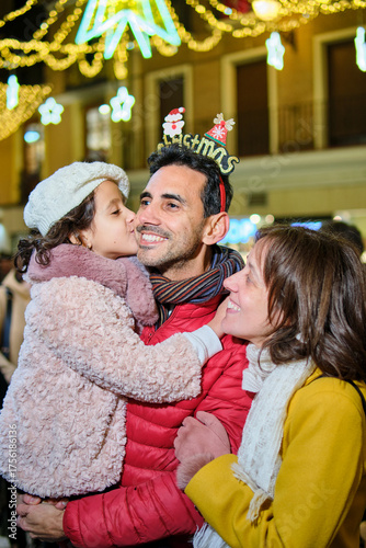 Vertical shot of parents with daughter kissing father at Christmas