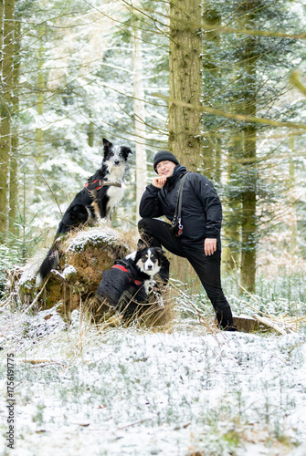 schwarz gekleideter Mann Hundebesitzer mit zwei Hunden Border Colli in tricolor und Merle odd-eyed  im Wald posierend auf einer Erhöhung