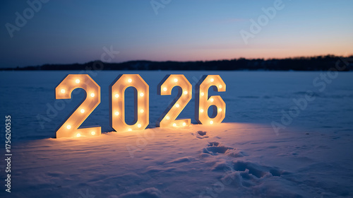 A 2026 illuminated marquee number illuminates a snowy landscape at twilight, surrounded by a serene frozen lake and distant dark treeline under a pastel evening sky.