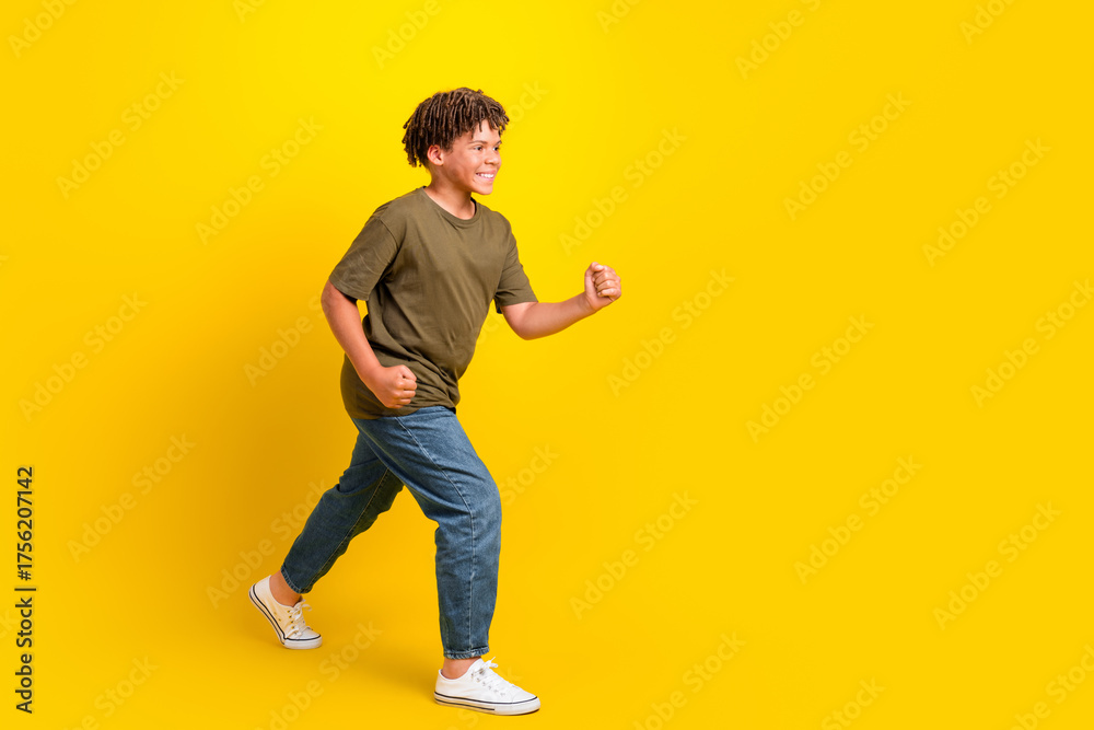 Fototapeta premium Funny energetic boy in casual khaki tee and jeans runs across a bright yellow background for a lively lifestyle and fitness style promo