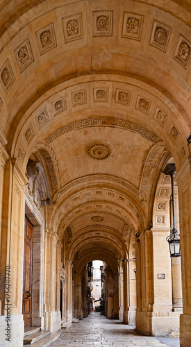 Historic vaulted corridor with patterned ceiling, arches and hanging lanterns in warm stone architecture