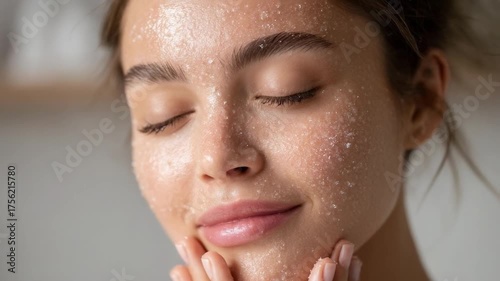 A woman with a facial exfoliating scrub on her face, eyes closed and hands cupping her cheeks.