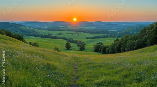 Panoramic view of a green meadow at sunset with rolling hills and distant valleys.
