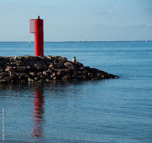 small red lighthouse at the end of the breakwater in the sea