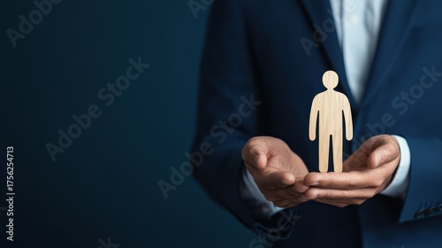 A business professional holds a wooden figure symbolizing care, support, or mentorship in a dramatic, dark setting.
