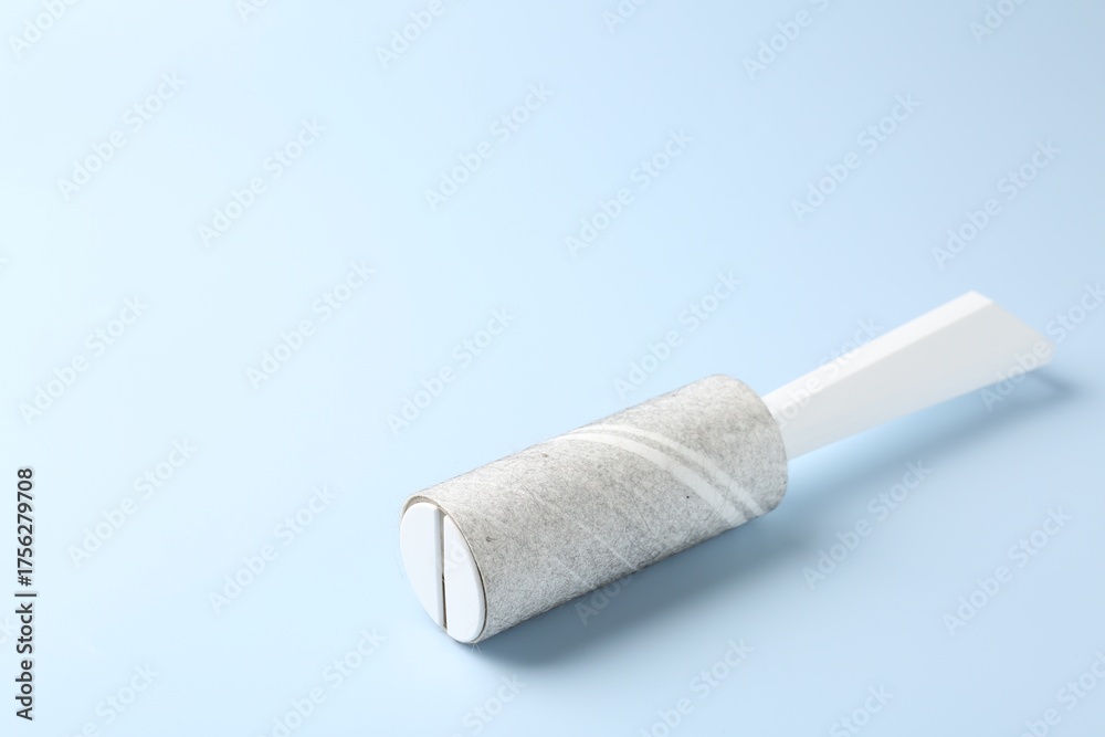 Obraz premium Lint roller with used sticky tape on light blue background, closeup. Space for text