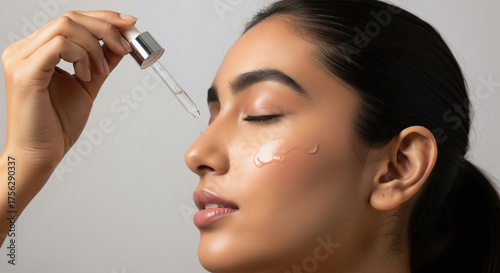 Beautiful woman applies facial serum for radiant, healthy skin.