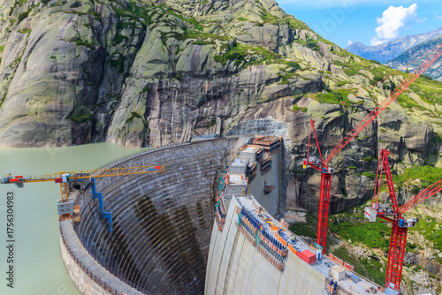 Scenic view of construction site with red cranes of new dam with lake at Swiss mountain pass Grimsel