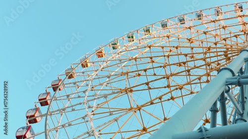 Bright colorful Ferris wheel under clear blue sky in evening sunlight. Urban summer leisure concept, amusement park landmark and joyful travel experience with panoramic city views.