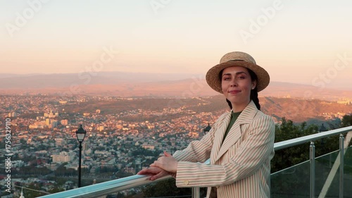 A young elegant Caucasian woman stands on a scenic viewpoint, admiring the panoramic city at sunset. Summer vacation, peaceful travel moments, and a love for beautiful destinations