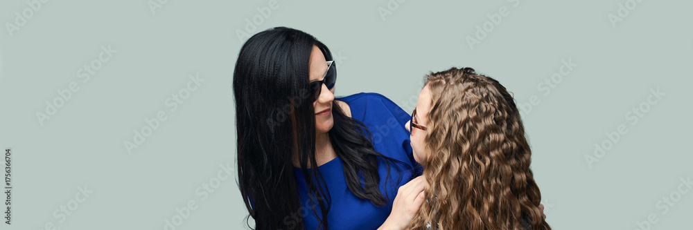 Fototapeta premium Caucasian adult female with black hair and child with curly hair smiling against plain background.