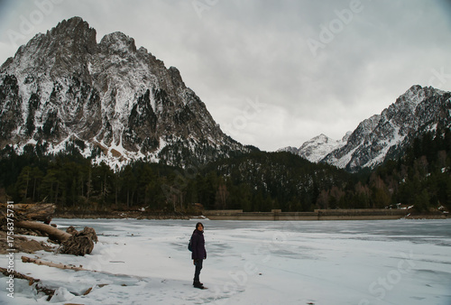 Girl hiking while observing Los Encantados, or Els Encantats in Catalan. These are two peaks that rise above the frozen lake of Sant Maurici. In Agüestortes National Park, Spain.