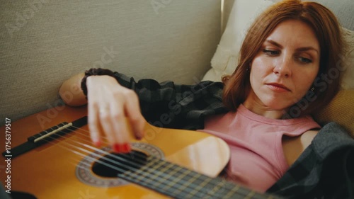 Woman playing guitar while relaxing on a couch in a cozy indoor setting during daytime