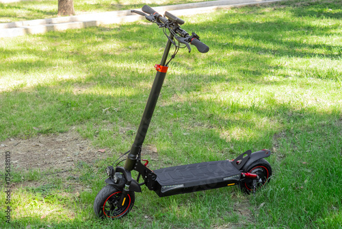 Black electric scooter with red accents parked on grassy surface, scooter concept