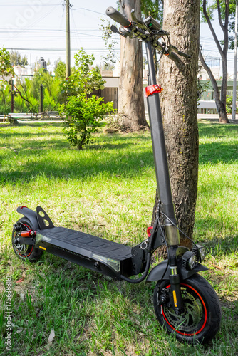 Electric scooter parked near tree in sunlit grassy park setting, electric scooter concept
