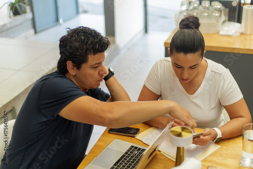 Dos colegas latinos colaborando en un proyecto de negocios en una oficina moderna, revisando documentos y usando tecnología.