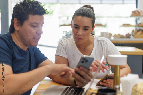 Pareja de negocios latina colaborando en un smartphone en una cafetería moderna.