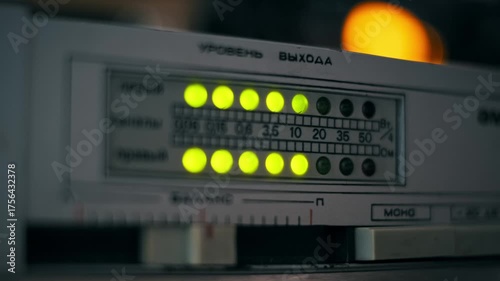 Low-light close-up of a retro audio amplifier's blinking LED level meter showing yellow-green sound indicators with a warm bokeh light in the background labeled with Cyrillic text for Output Level.