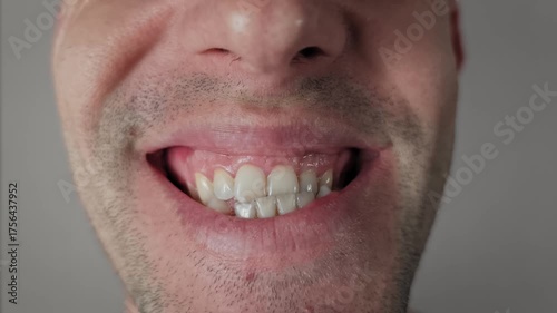 Extreme close up shot of an unshaven male face puckering lips for a kiss then relaxing. The shot shows pink lip texture and dark stubble against a neutral grey studio background.