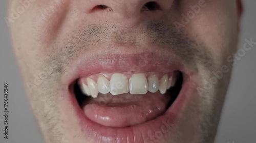 Macro shot of a man with stubble making funny faces, sticking his tongue out, rolling and folding it in unusual ways. He shows his crooked teeth in a goofy, playful, and comical expression.