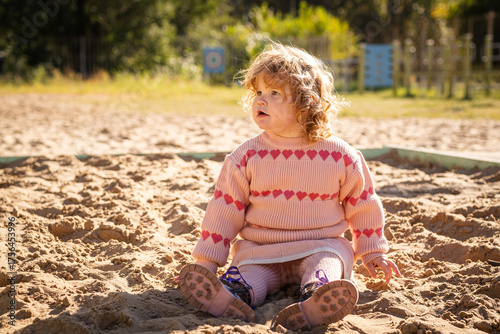 Child playing in sandy area wearing warm sweater on a bright sunny day outdoors