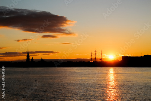 Silhouettes of city buildings against the backdrop of the setting sun, reflected in the waters of the river