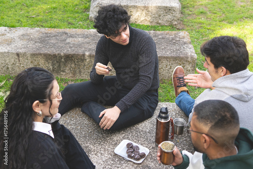 Happy university students relaxing on the grass with yerba mate and snacks