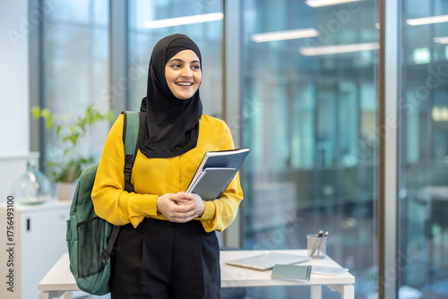 Canvastavla Young muslim woman smiling, carrying a backpack and holding notebooks, standing
