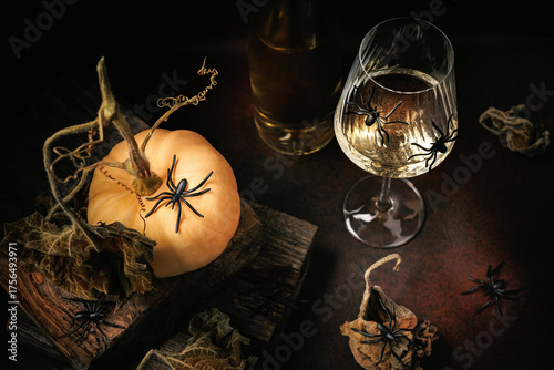 Top view of pale pumpkin with spiders, wine glass and dried leaves arranged in Halloween themed still life
