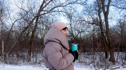 Wallpaper Mural A woman in a warm down jacket drinks hot tea from a thermal cup in the winter forest. A walk in the park, forest in winter. Snowy cold winter. Torontodigital.ca