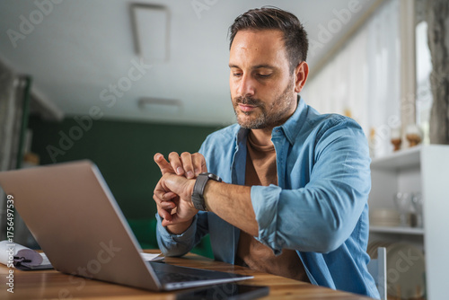 Bilde på lerret Man using smart watch checking time working with laptop