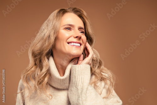 Portrait of a smiling mature woman in a stylish beige sweater, radiating beauty and confidence