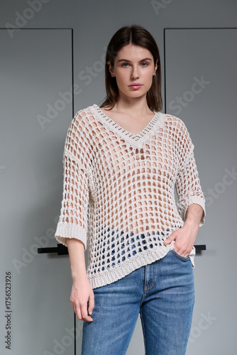 A girl model in stylish clothes poses on a gray background.