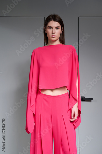 A girl model in stylish clothes poses on a gray background.