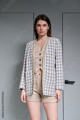 A girl model in stylish clothes poses on a gray background.